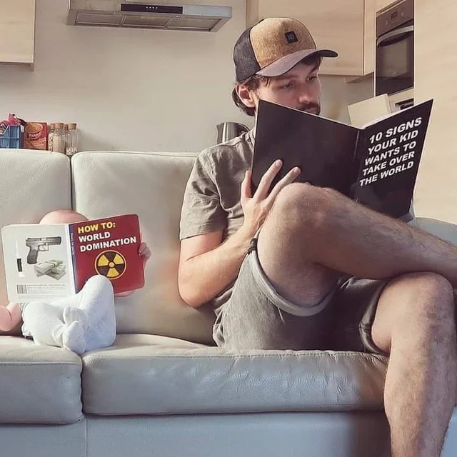 Funny photo of a dad reading “10 Signs Your Kid Wants to Take Over the World” next to a baby reading about world domination — top 20 funny images online.