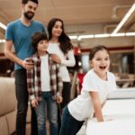 Happy family buys new orthopedic mattress in furniture store. Blissful family choosing mattresses in store.