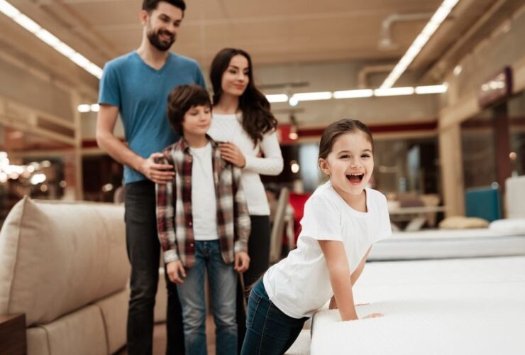 Happy family buys new orthopedic mattress in furniture store. Blissful family choosing mattresses in store.