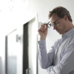 Man holding eyeglasses with a thoughtful, stressed look