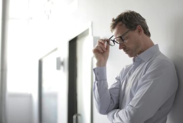 Man holding eyeglasses with a thoughtful, stressed look