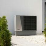 Outdoor air conditioning unit beside modern home with plants
