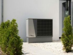Outdoor air conditioning unit beside modern home with plants