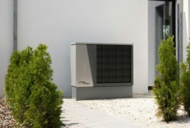 Outdoor air conditioning unit beside modern home with plants