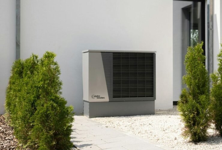 Outdoor air conditioning unit beside modern home with plants