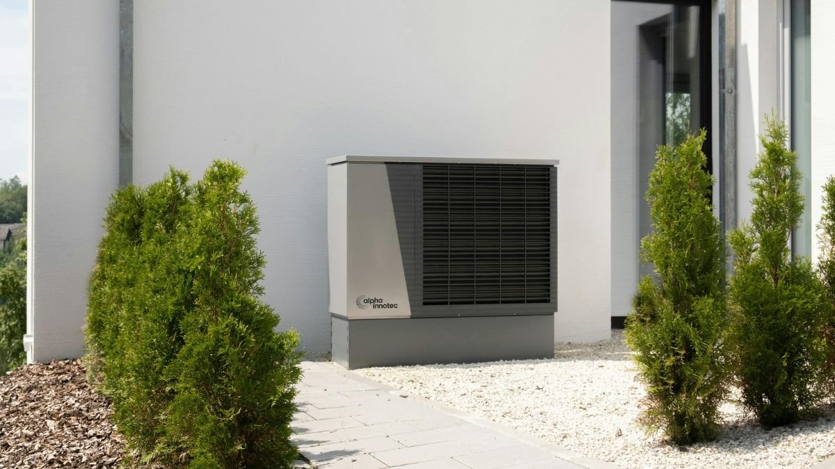 Outdoor air conditioning unit beside modern home with plants