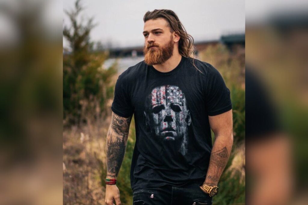 Jake the Viking, a former MrBeast crew member, walks outdoors in a black t-shirt with a Michael Myers design. Known for his towering height of 6'5.6" (197 cm), he was one of the tallest members of the MrBeast team before leaving in 2020.