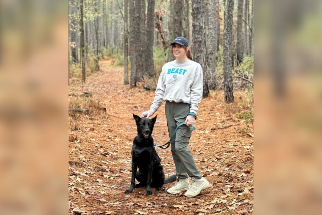 Krist Tyson, former MrBeast crew member, enjoys a peaceful hike in the woods with her black dog, wearing a ‘Beast’ sweatshirt.