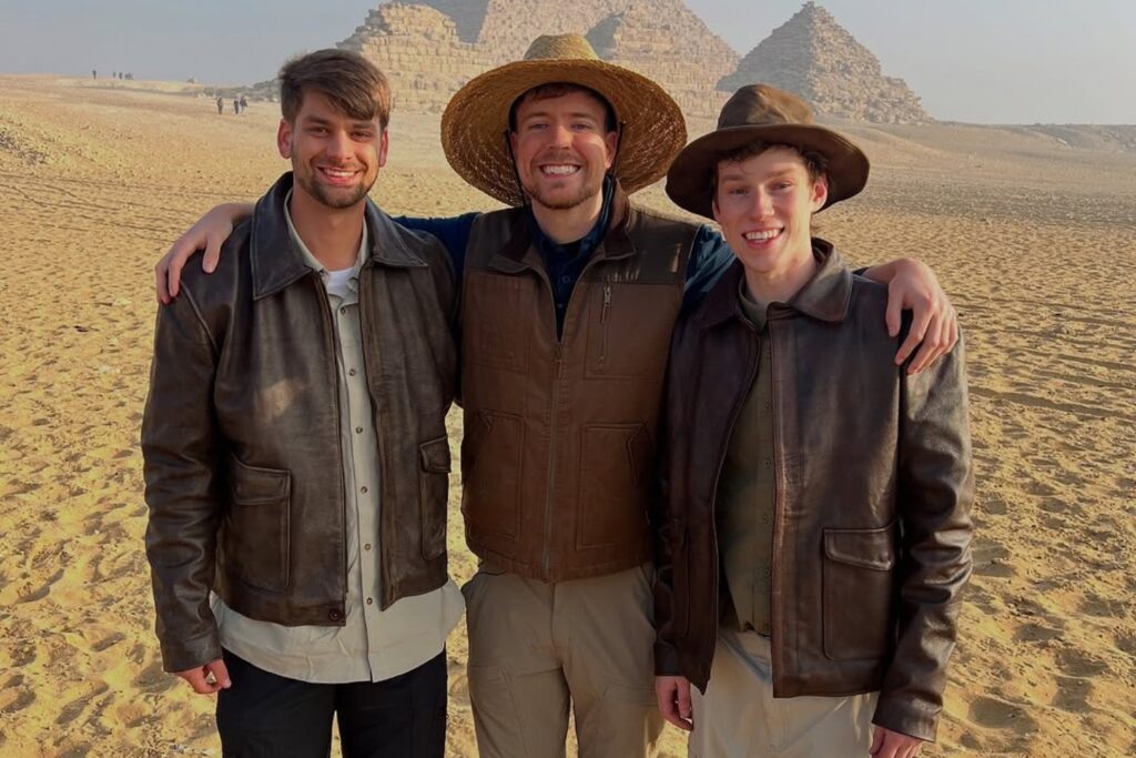 MrBeast, Chandler Hallow, and a crew member in leather jackets posing in front of the pyramids, highlighting their height differences.