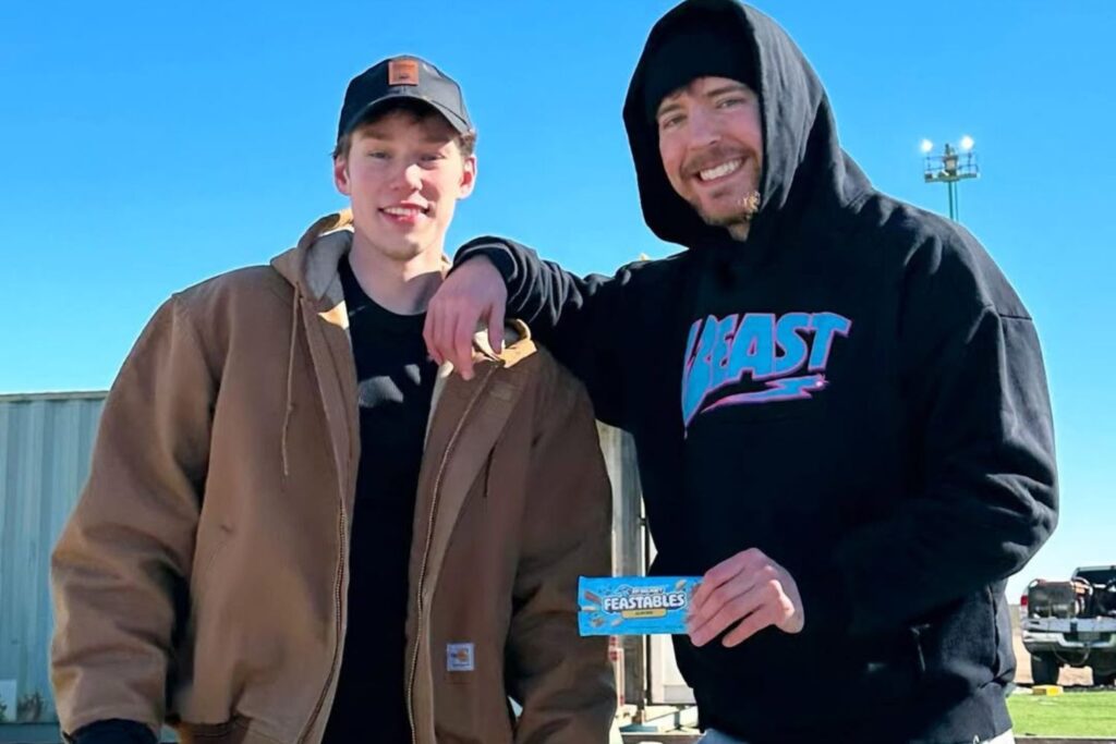 MrBeast and Nolan Hansen pose outdoors, holding Feastables chocolate bars, with Nolan leaning on MrBeast’s shoulder, highlighting their height difference.