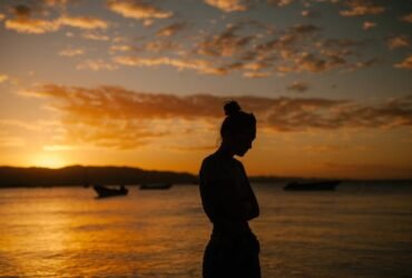Photo by Julia Volk - Sad woman suffering with mental health standing on coast of sea at sunset