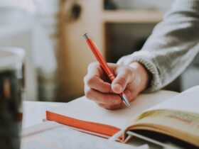 Child holding an orange pen while writing, symbolizing creative writing prompts for first graders.