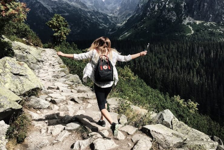 Woman standing on a cliff, embracing the adventure of a travel-based job.