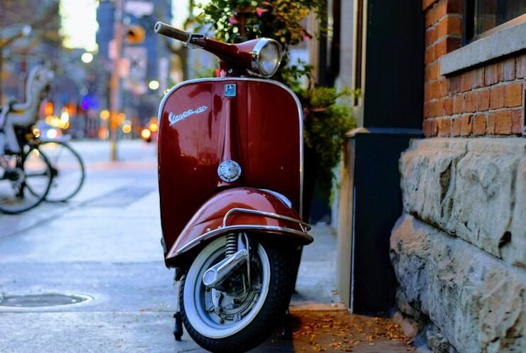 A red Piaggio Vespa scooter parked in an urban setting, showcasing modern mobility design.