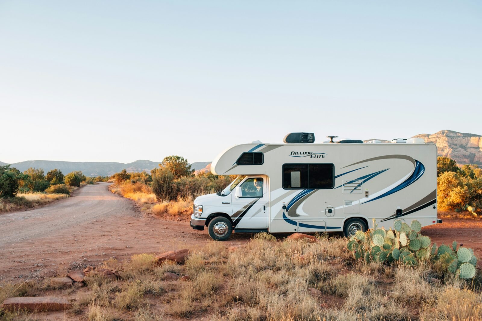 White and brown RV parked on an open field under clear daylight, symbolizing freedom and adventure on the open road.